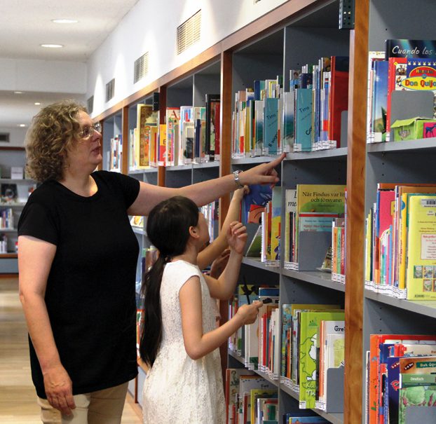 Birgit Thomsmeier hilft einem Mädchen, ein Buch im großen Bücherregal zu finden. Foto: Hensel