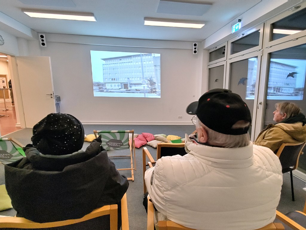 Ausstellungsbesucher sehen einen Film mit historischen Aufnahmen an. Foto: Hensel