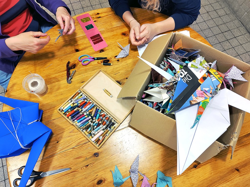 Die Papier-Kraniche werden mit Schnüren versehen. Foto: Hensel