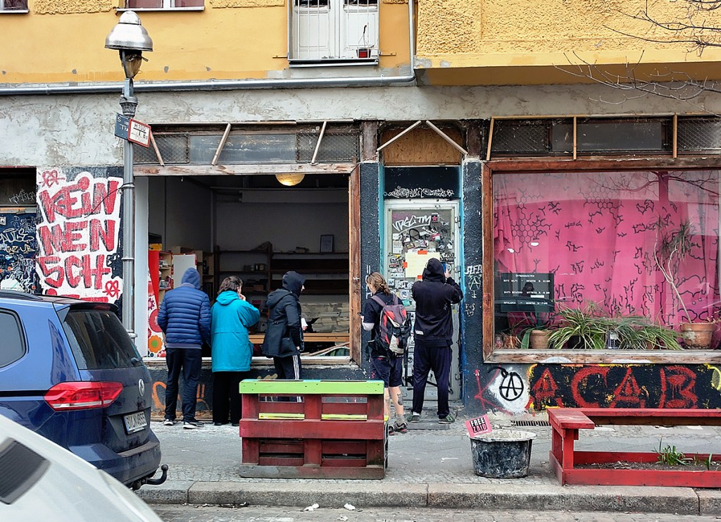 Passanten und Bewohner schauen sich die eingeschlagene Scheibe des Infoladens an. Foto: Hensel