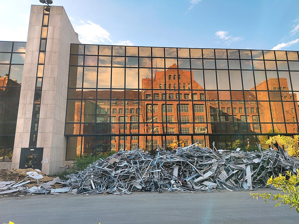 Ehemals von der AEG genutztes Gebäude spiegelt sich in der alten Nixdorf-Fabrik. Davor, eine Berg mit geborgenen Rohstoffen. Foto: Hensel