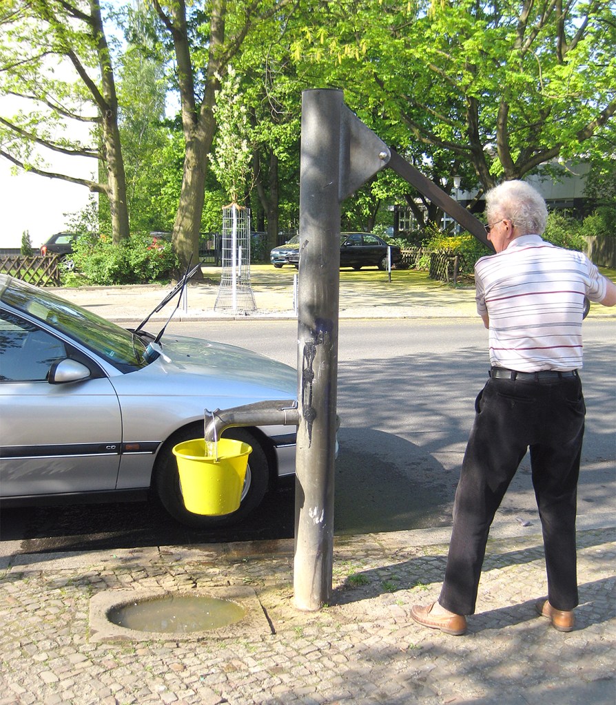 Mann pumpt Wasser aus einem Straßenbrunnen in einen gelben Eimer