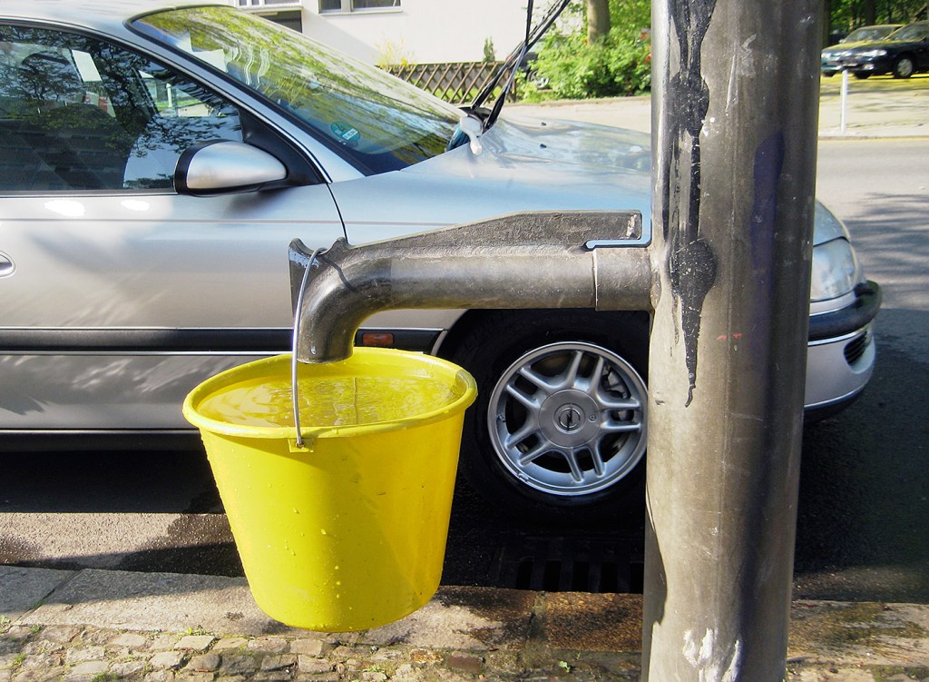 Gelber Eimer hängt an einer Berliner Straßenpumpe