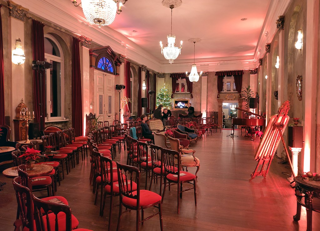 Großer Saal im Ballhaus Wedding mit Reihen von Stühlen und warmem Licht.