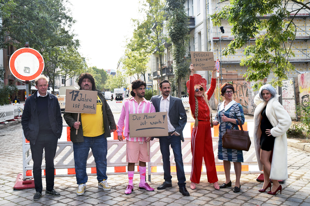 Schauspielerinnen und Schauspieler des Prime Time Theaters mit Schildern bei der Wiedereröffnung der Burgsdorfstraße in Berlin-Wedding