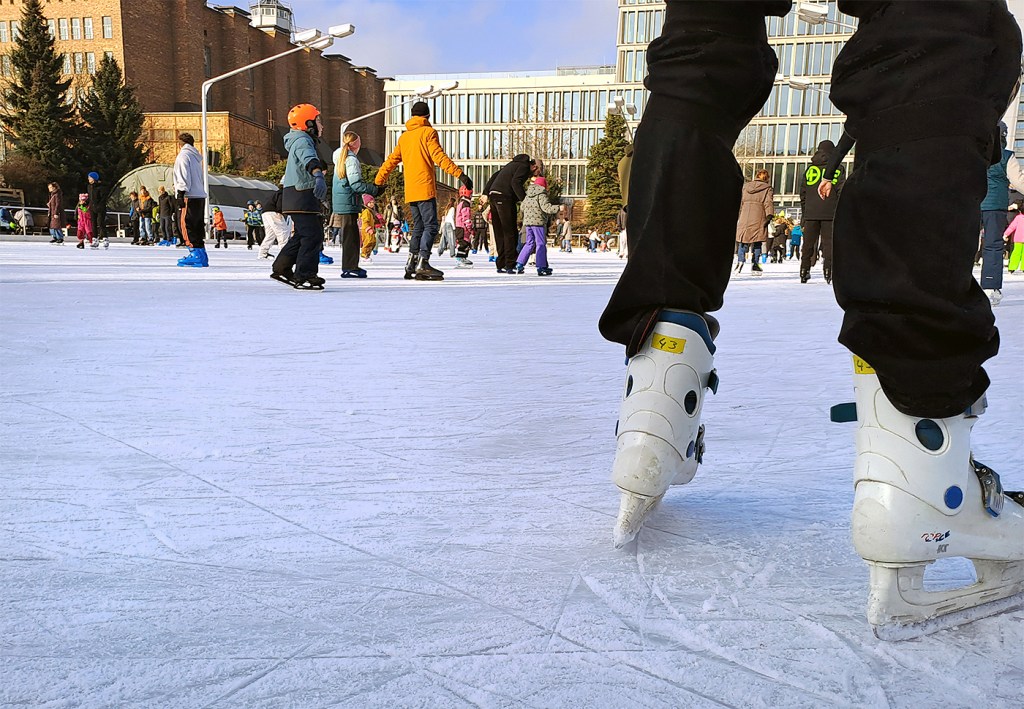 Schlittschuhe im Vordergrund, dahinter Kinder und Erwachsene auf der Außenfläche des Erika-Heß-Eisstadions im Wedding.