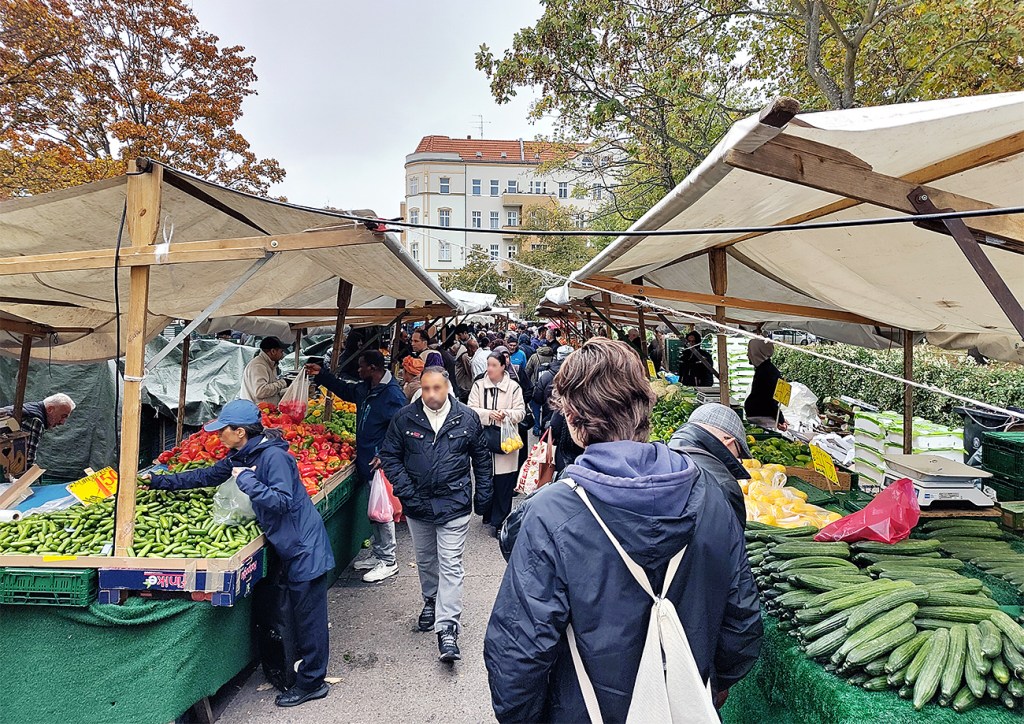 Viele Menschen gehen zwischen Gemüse-Marktständen auf dem Genter Wochenmarkt hindurch.