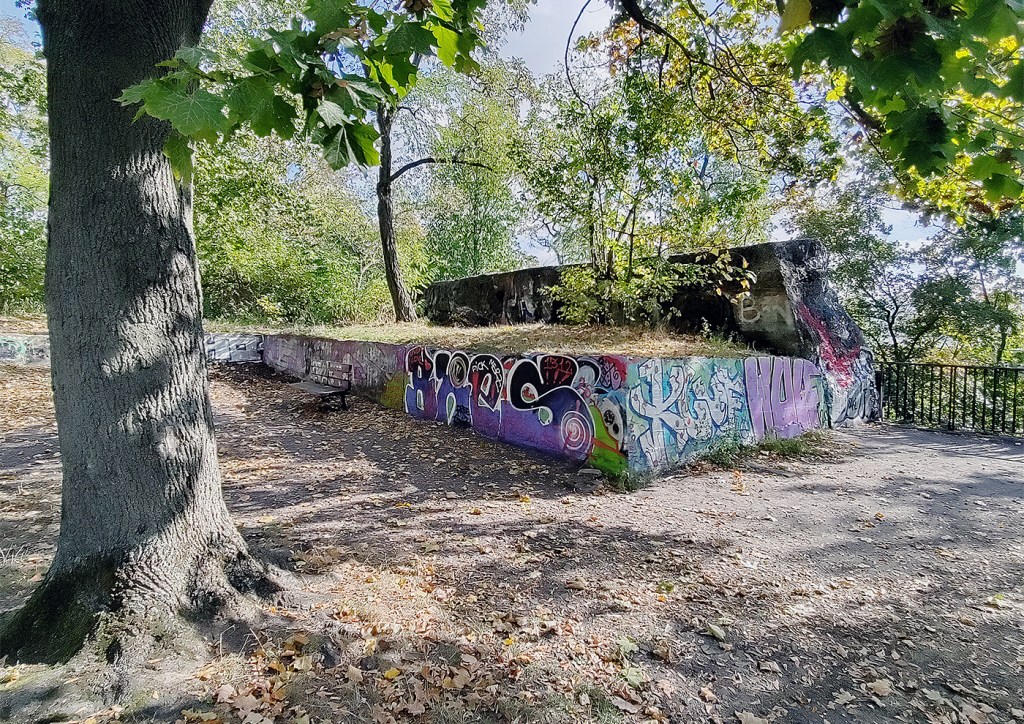 Betonreste des ehemaligen Leitturmbunkers im Humboldthain, umgeben von Bäumen und herbstlichem Grün.