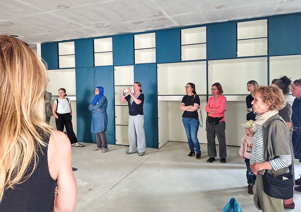 Besucherinnen und Besucher stehen bei einer Baustellenführung im neuen Anbau des Olof-Palme-Zentrums vor einer Wand mit blauen Einbauschränken.