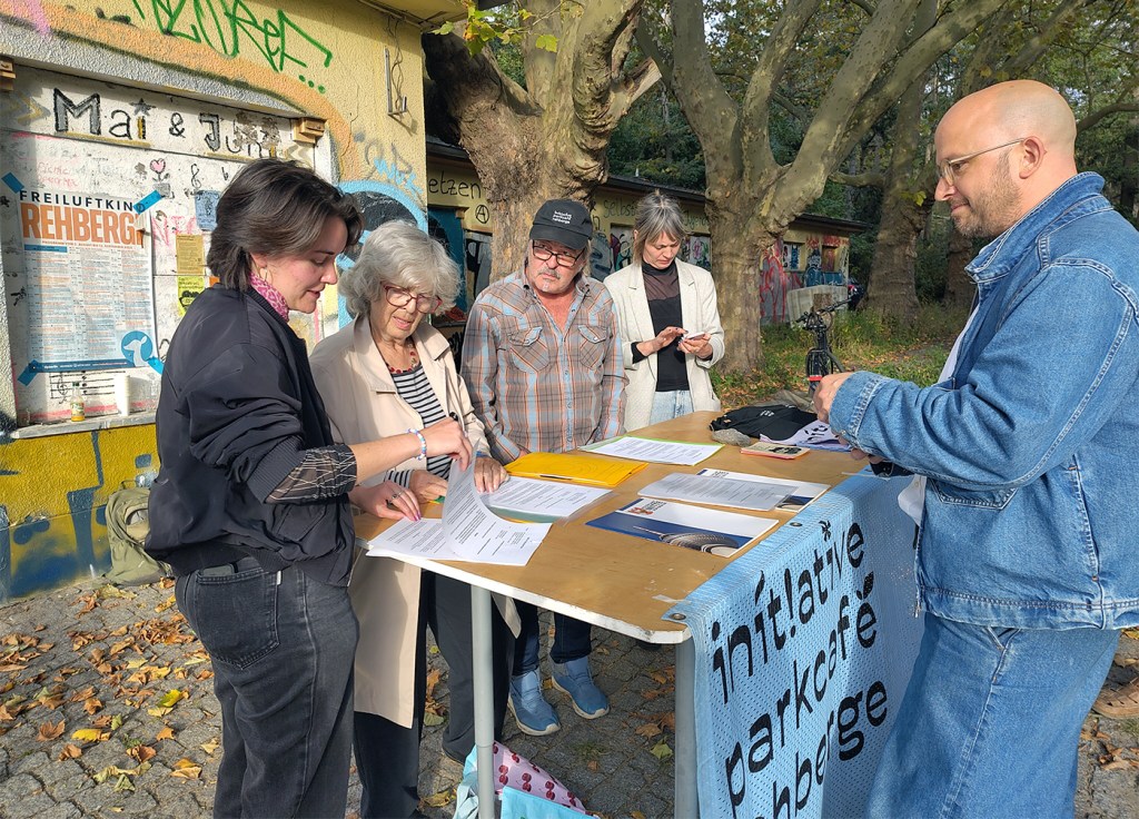 Vertreter des Vereins Parkcafé Rehberge und Bezirksstadtrat Christopher Schriner bei der Vertragsunterzeichnung an einem Tisch vor dem Parkcafé.